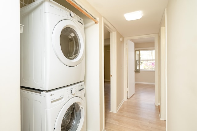 laundry room with stacked washer / drying machine, baseboards, light wood-style floors, and laundry area