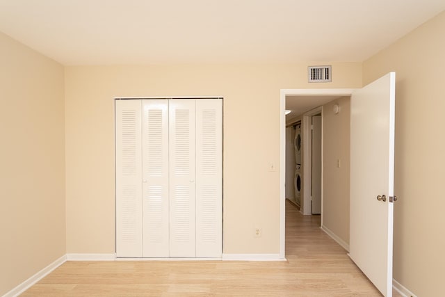 unfurnished bedroom featuring light wood-type flooring, visible vents, baseboards, and stacked washing maching and dryer