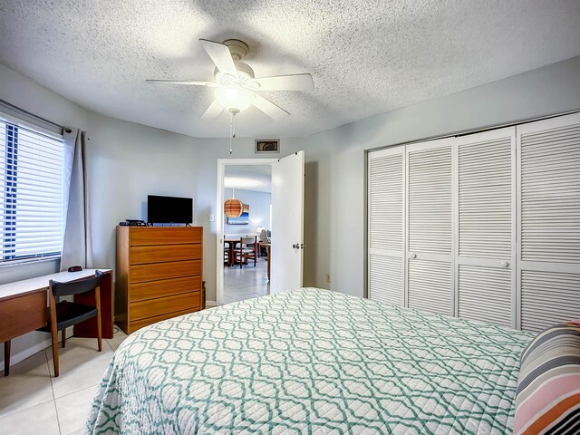 bedroom with a textured ceiling, a closet, ceiling fan, and light tile patterned flooring