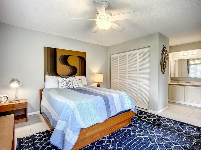 tiled bedroom with connected bathroom, ceiling fan, sink, a textured ceiling, and a closet