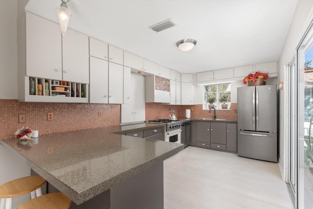 kitchen with appliances with stainless steel finishes, white cabinets, a kitchen bar, and kitchen peninsula