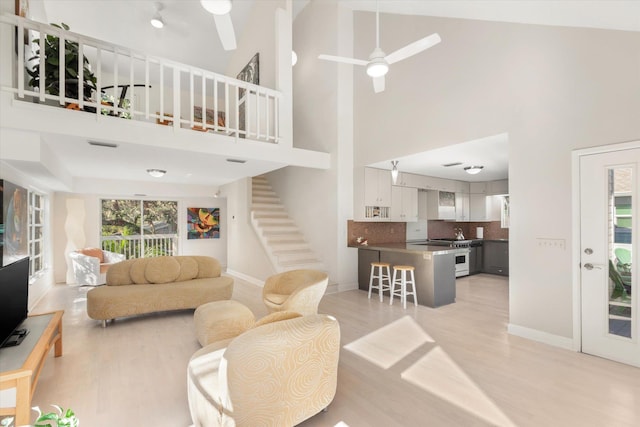 living room with ceiling fan, a high ceiling, and light wood-type flooring