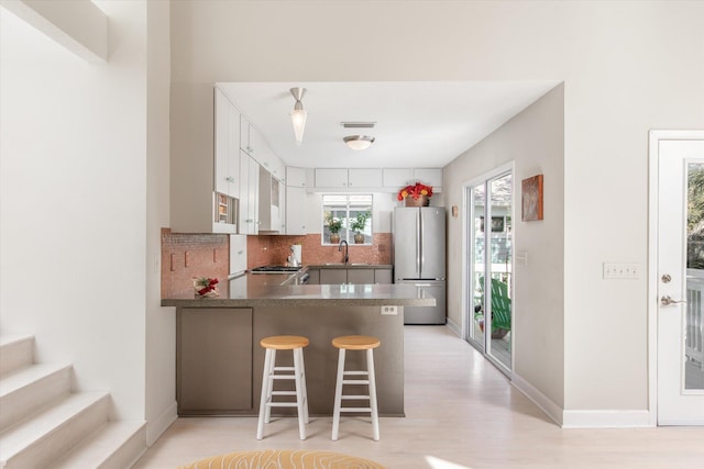 kitchen with sink, a kitchen breakfast bar, stainless steel fridge, kitchen peninsula, and decorative backsplash