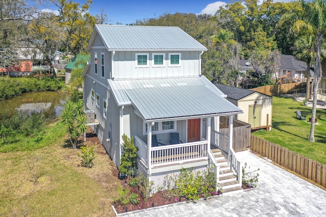 view of front of house with a front yard, fence, covered porch, board and batten siding, and metal roof