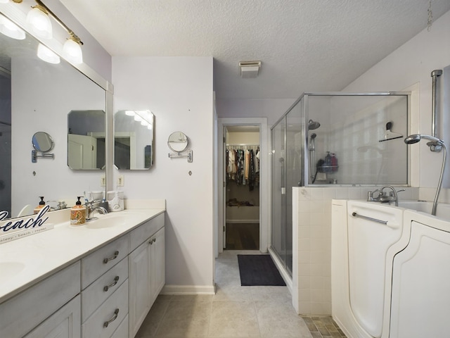 bathroom with vanity, a textured ceiling, washer / clothes dryer, a shower with shower door, and tile patterned floors