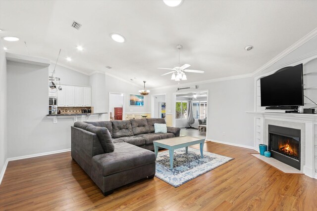 living room with lofted ceiling, a tiled fireplace, ceiling fan, crown molding, and dark wood-type flooring