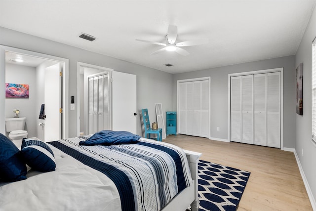 bedroom with baseboards, wood finished floors, visible vents, and multiple closets