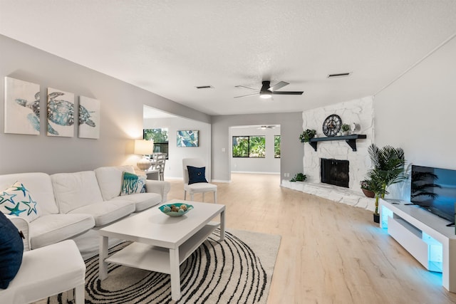 living area with a fireplace, visible vents, ceiling fan, a textured ceiling, and light wood-type flooring