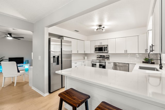 kitchen featuring visible vents, backsplash, appliances with stainless steel finishes, light wood-type flooring, and a peninsula