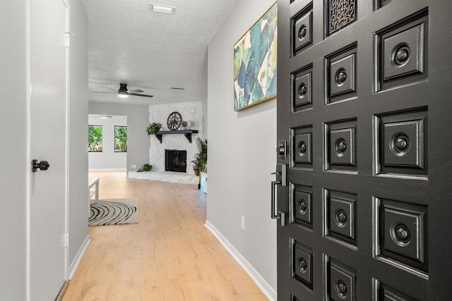 foyer with visible vents, a ceiling fan, a stone fireplace, a textured ceiling, and wood finished floors