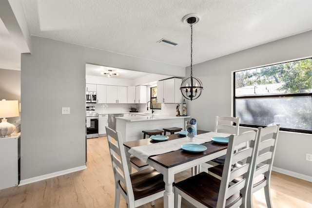 dining room featuring light wood-style flooring, a textured ceiling, visible vents, and baseboards