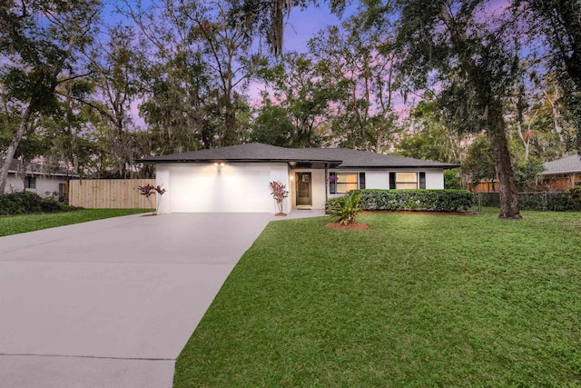 ranch-style house featuring a garage, fence, concrete driveway, stucco siding, and a front yard