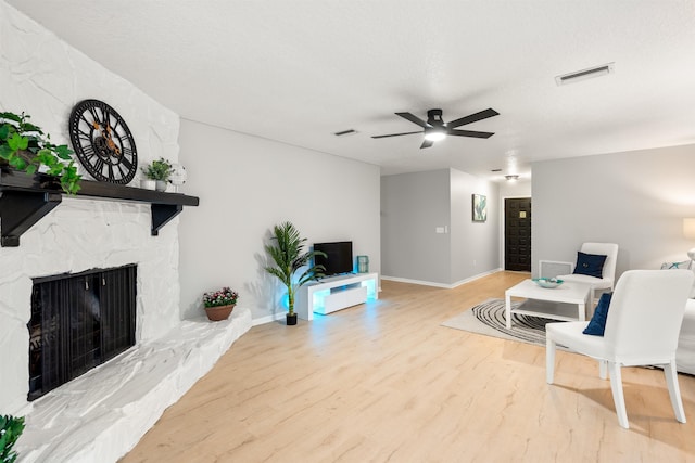 living room featuring a fireplace, visible vents, a ceiling fan, wood finished floors, and baseboards