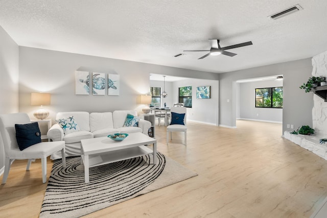 living area with light wood-style floors, visible vents, a ceiling fan, and a stone fireplace