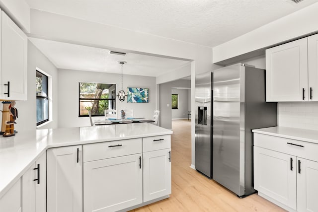 kitchen with a peninsula, light countertops, white cabinetry, and stainless steel fridge with ice dispenser