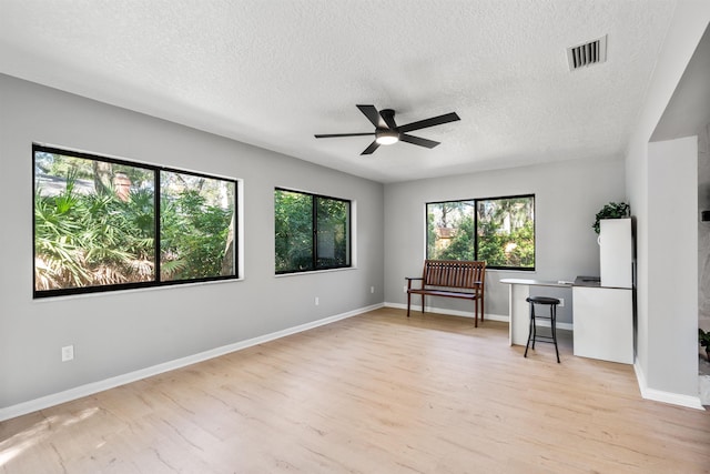 unfurnished room with baseboards, visible vents, a ceiling fan, light wood-style flooring, and a textured ceiling