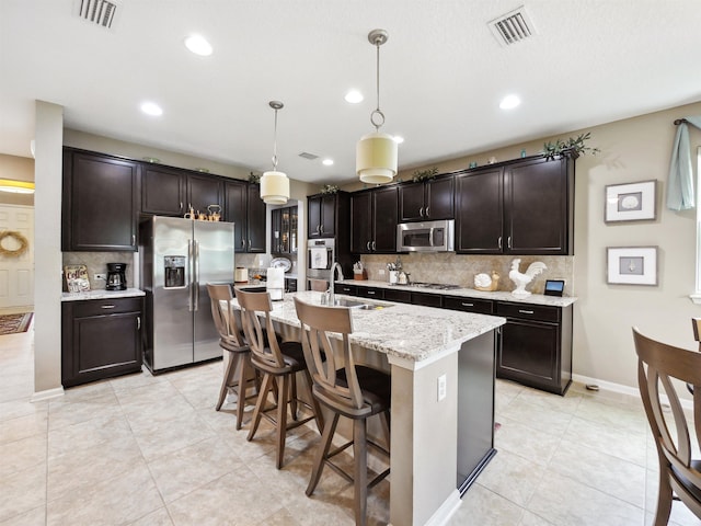 kitchen with a kitchen island with sink, sink, decorative backsplash, appliances with stainless steel finishes, and decorative light fixtures