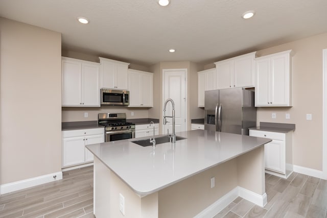 kitchen with white cabinets, stainless steel appliances, a kitchen island with sink, and sink