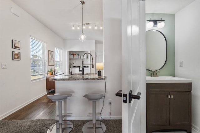 kitchen featuring sink, decorative light fixtures, a breakfast bar area, dark brown cabinets, and dark hardwood / wood-style flooring