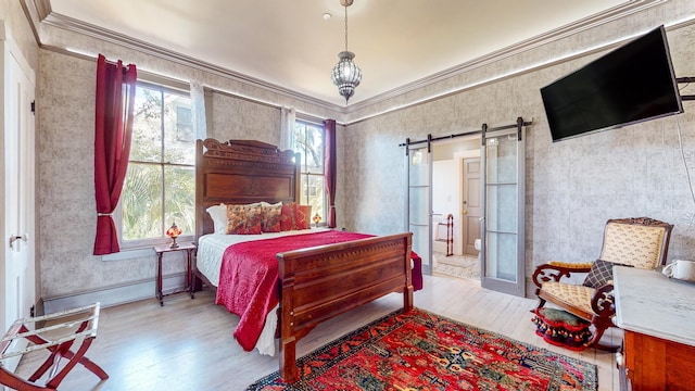 bedroom featuring a barn door, ornamental molding, and light wood-type flooring