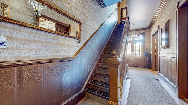 stairs featuring carpet flooring, crown molding, a towering ceiling, and a chandelier