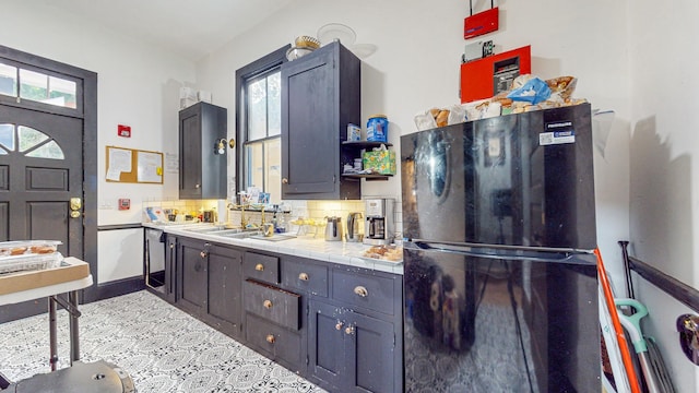 kitchen featuring backsplash, tile counters, black refrigerator, and sink