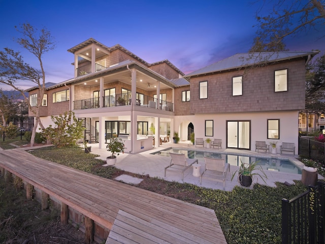 back house at dusk featuring a balcony, a patio area, and a fenced in pool