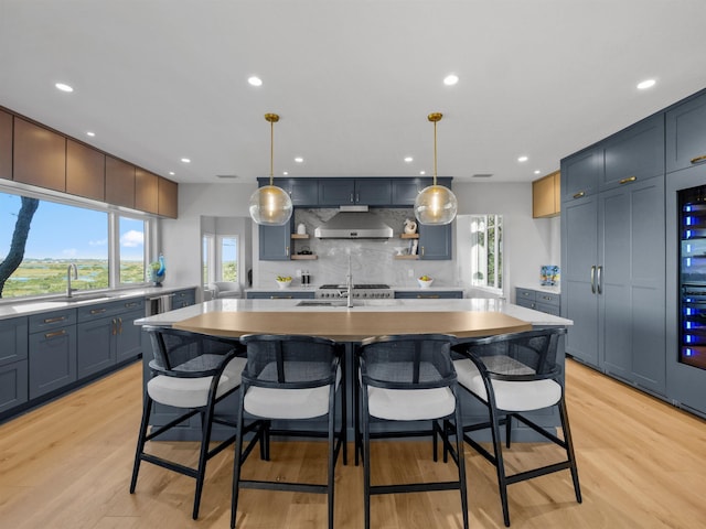 kitchen featuring pendant lighting, light wood-type flooring, tasteful backsplash, a kitchen island with sink, and a breakfast bar