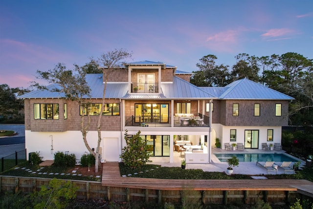 back house at dusk featuring a balcony and a patio