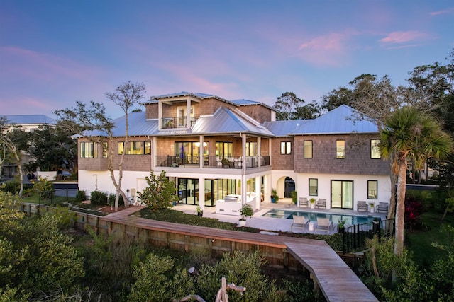 back house at dusk featuring a balcony and a patio