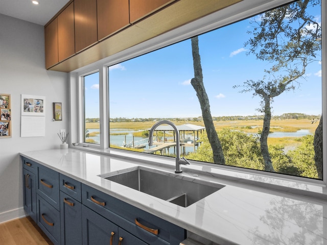 kitchen featuring sink, light hardwood / wood-style floors, a water view, and light stone counters