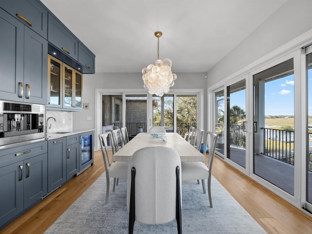 dining space featuring sink, light wood-type flooring, a water view, an inviting chandelier, and beverage cooler