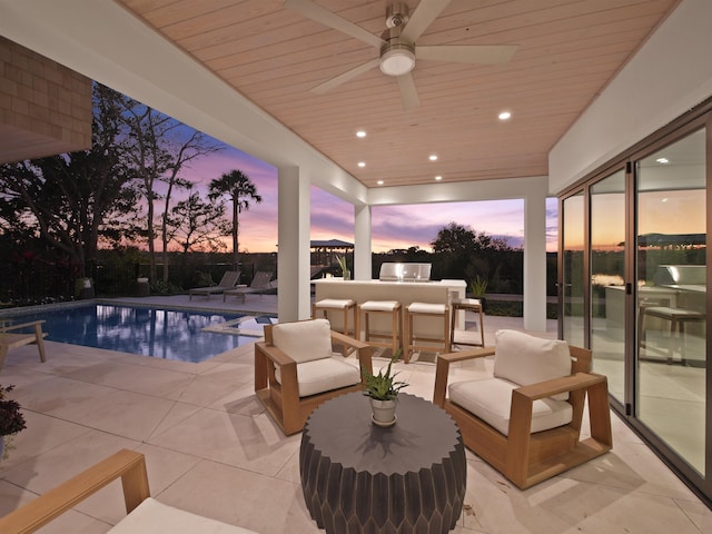 patio terrace at dusk with ceiling fan, a fenced in pool, and a bar