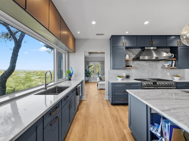 kitchen with wall chimney range hood, sink, backsplash, light stone counters, and range with two ovens