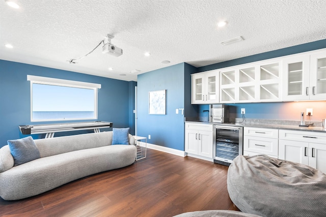 living room featuring beverage cooler, baseboards, dark wood-style flooring, indoor wet bar, and a textured ceiling