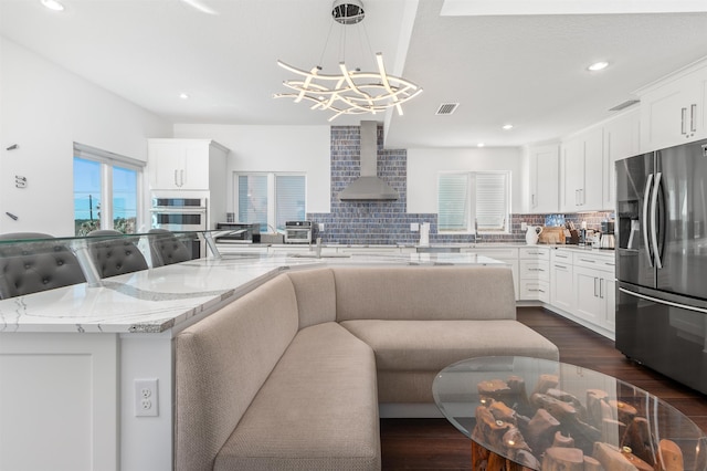 kitchen featuring decorative backsplash, stainless steel appliances, an inviting chandelier, white cabinetry, and wall chimney exhaust hood
