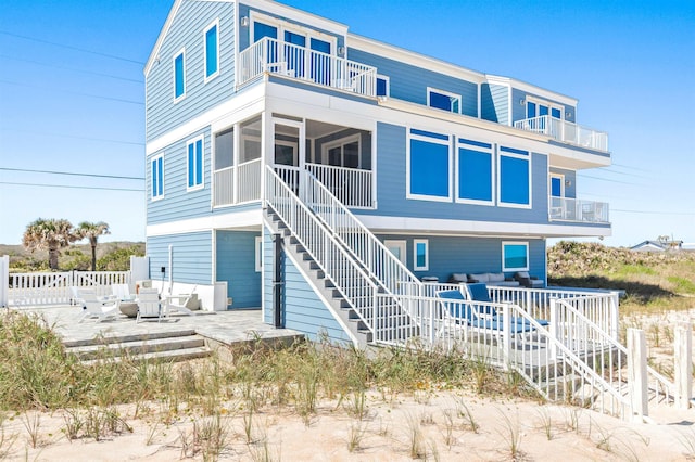 back of property featuring a patio, stairway, a balcony, fence, and a sunroom