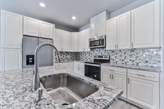 kitchen featuring light stone countertops, stainless steel appliances, white cabinetry, and sink