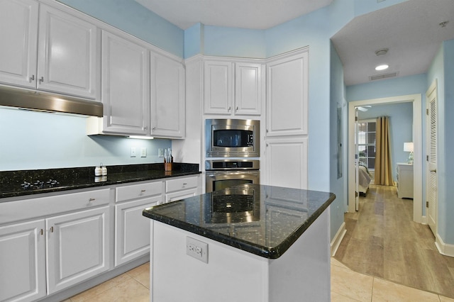 435 N Ocean Grande Dr Unit 104, Ponte Vedra Beach, FL 32082 - kitchen with appliances with stainless steel finishes, white cabinets, under cabinet range hood, dark stone countertops, and a center island