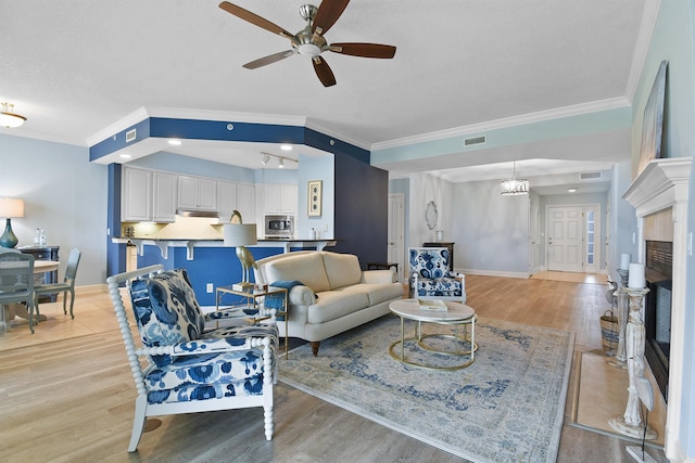 living room with ceiling fan with notable chandelier, crown molding, and light hardwood / wood-style flooring