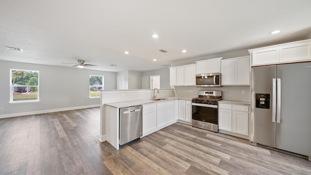 kitchen with kitchen peninsula, light wood-type flooring, stainless steel appliances, sink, and white cabinetry