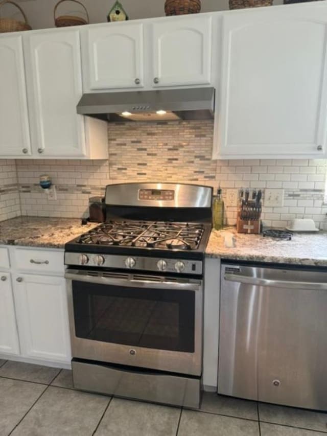 kitchen with light stone countertops, stainless steel appliances, white cabinetry, and light tile patterned flooring