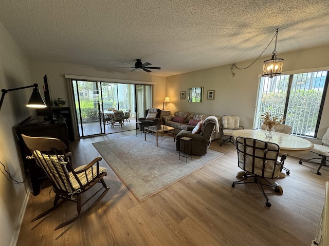 living room featuring wood-type flooring, ceiling fan with notable chandelier, and a textured ceiling