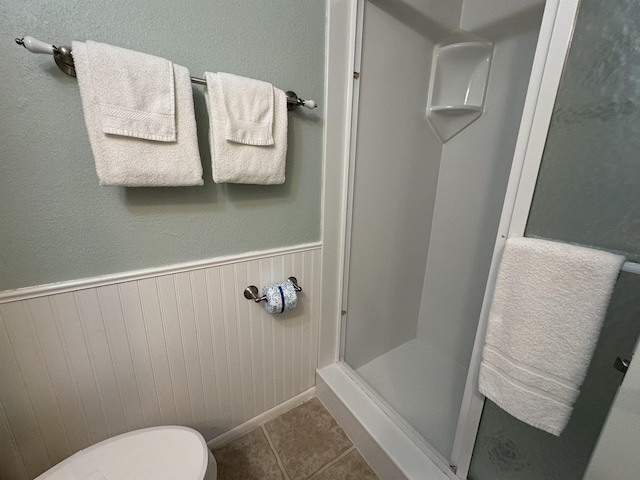 bathroom with toilet, a shower, and tile patterned flooring