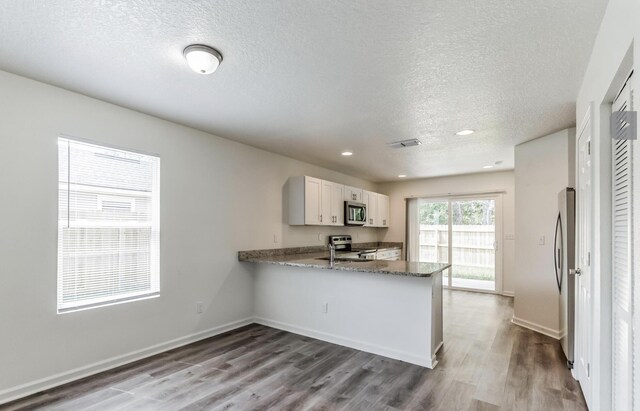 kitchen featuring light stone countertops, light hardwood / wood-style flooring, kitchen peninsula, white cabinets, and appliances with stainless steel finishes