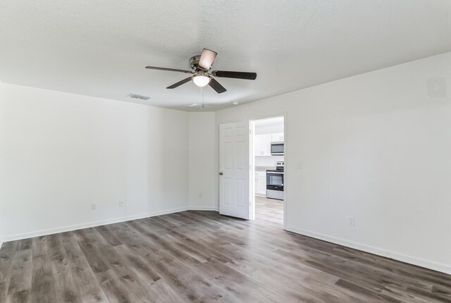 empty room with ceiling fan, wood-type flooring, and a textured ceiling