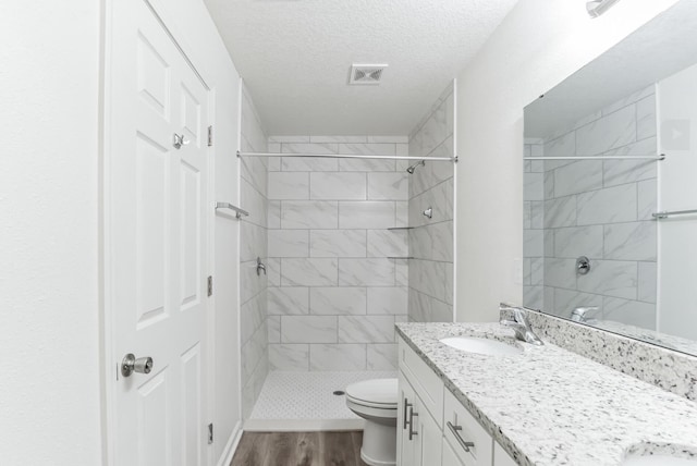 bathroom featuring a tile shower, hardwood / wood-style floors, a textured ceiling, toilet, and vanity