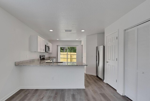 kitchen featuring light hardwood / wood-style floors, white cabinetry, kitchen peninsula, and stainless steel appliances