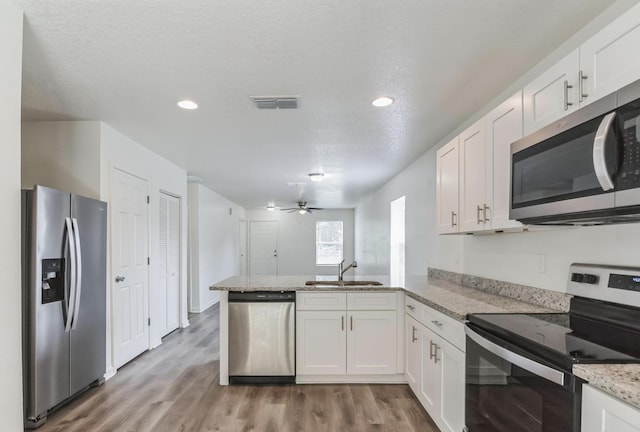 kitchen with kitchen peninsula, white cabinets, stainless steel appliances, and light hardwood / wood-style floors