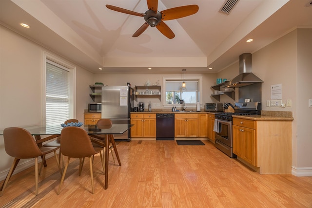 kitchen with decorative light fixtures, a tray ceiling, stainless steel appliances, light hardwood / wood-style floors, and wall chimney range hood